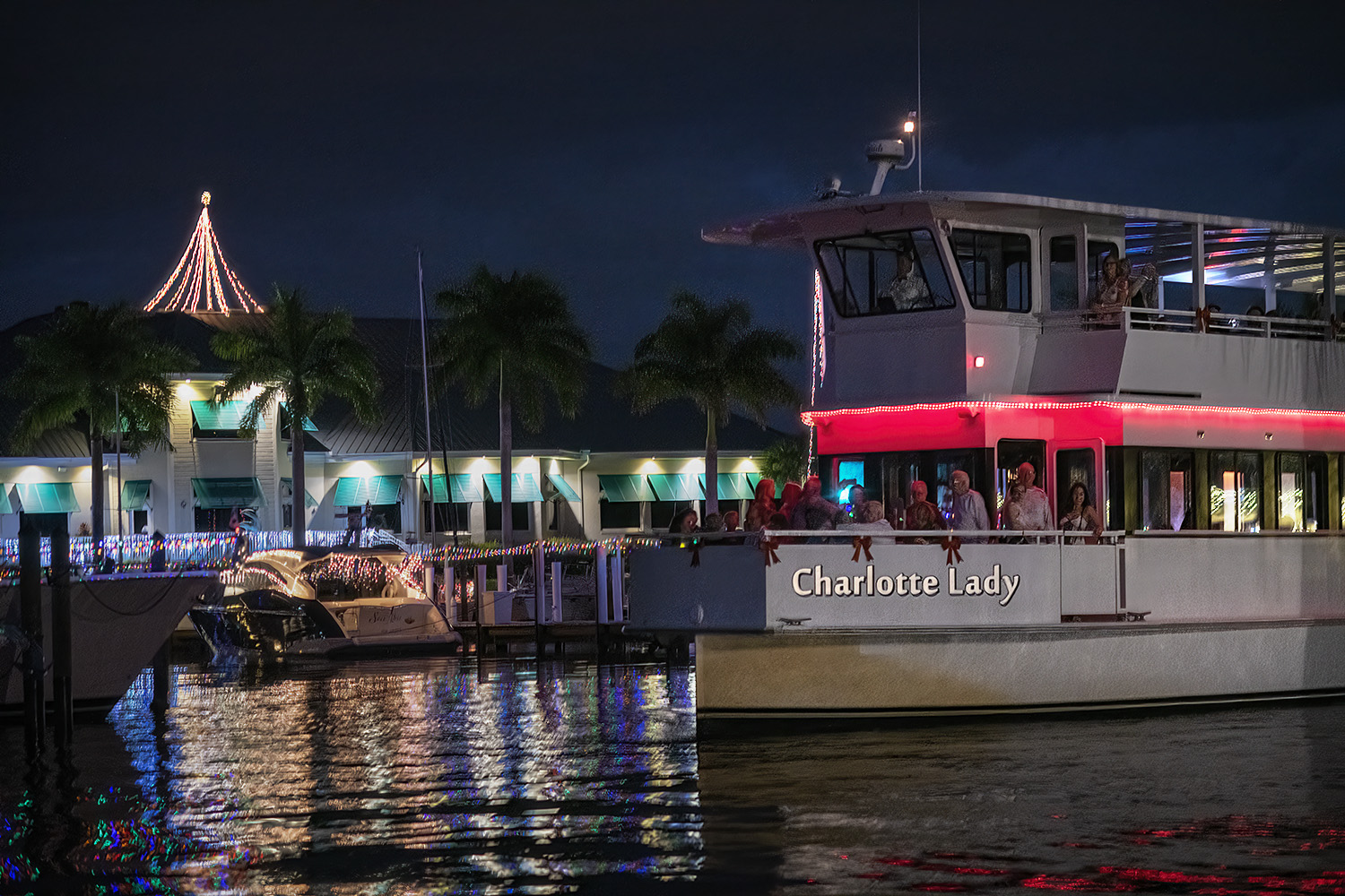 A boat named 'Charlotte Lady' lit up at night near a decorated marina.