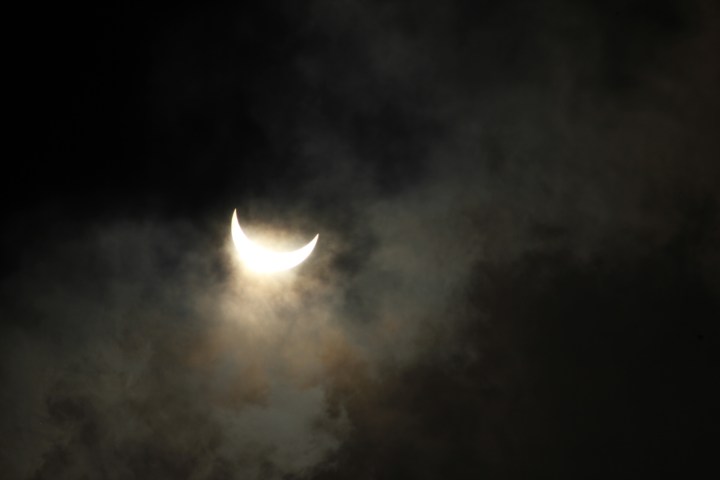Crescent-shaped sun during an eclipse, surrounded by dark clouds.